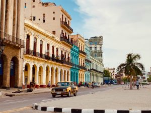 Vista de la avenida en La Habana Vieja con edificios coloniales de colores vibrantes y un automóvil clásico amarillo transitando la calle.